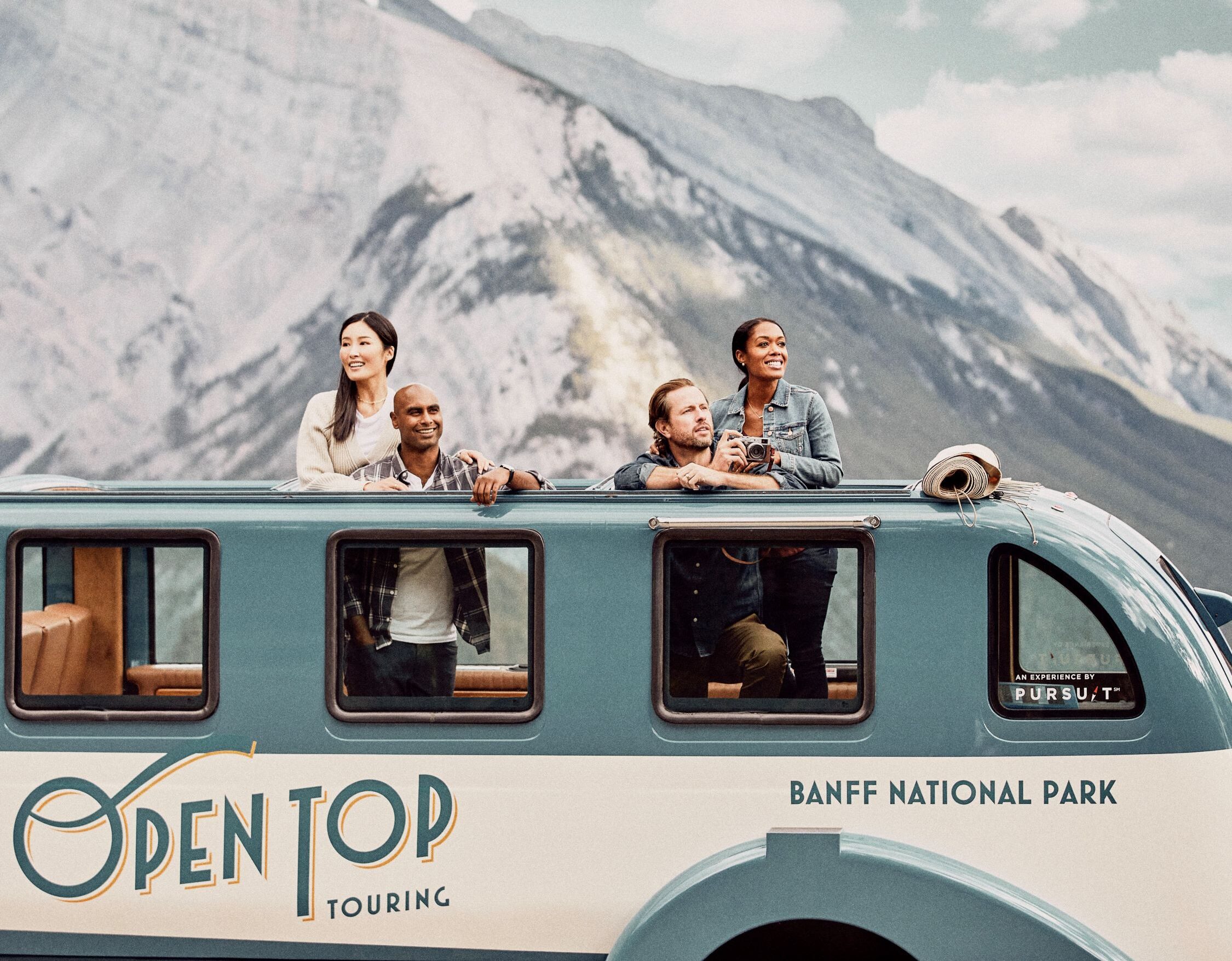 People in open top touring bus in front of mountains in Banff National Park.