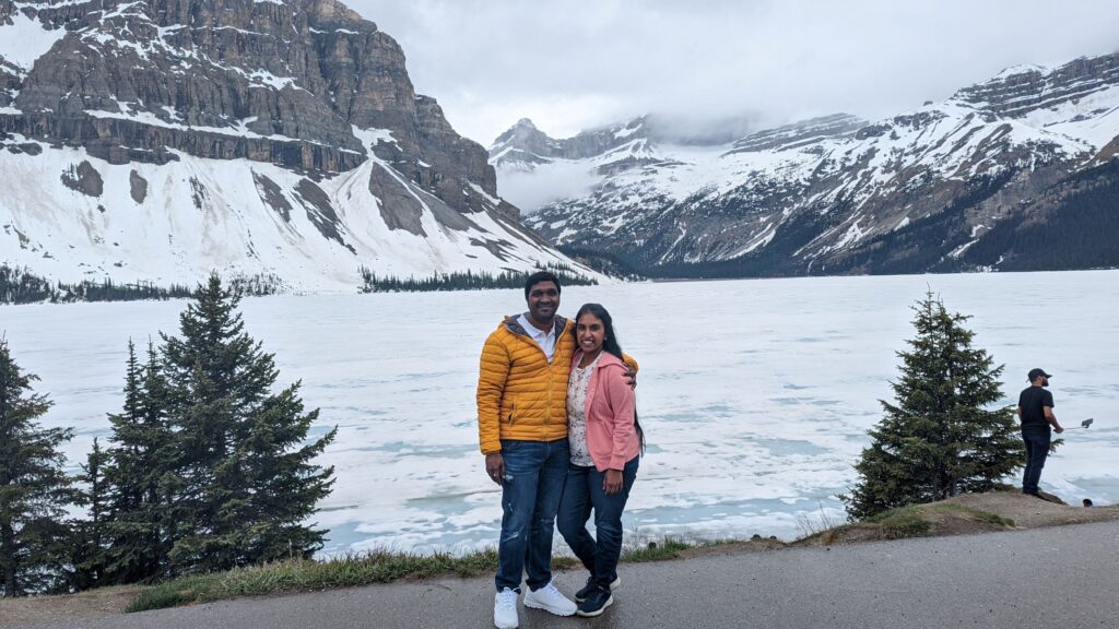 Photo of a couple standing in front of a lake covered in ice. How to plan a weekend trip to Banff