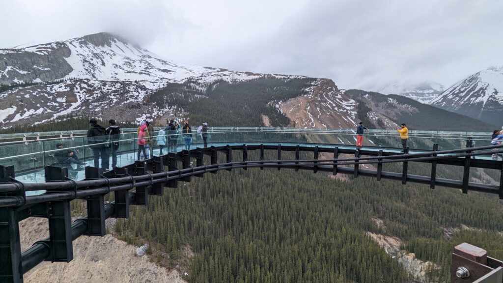 An image of the Columbia Icefields Skywalk over top of a mountains and forests with people standing on it.A Weekend in Banff.