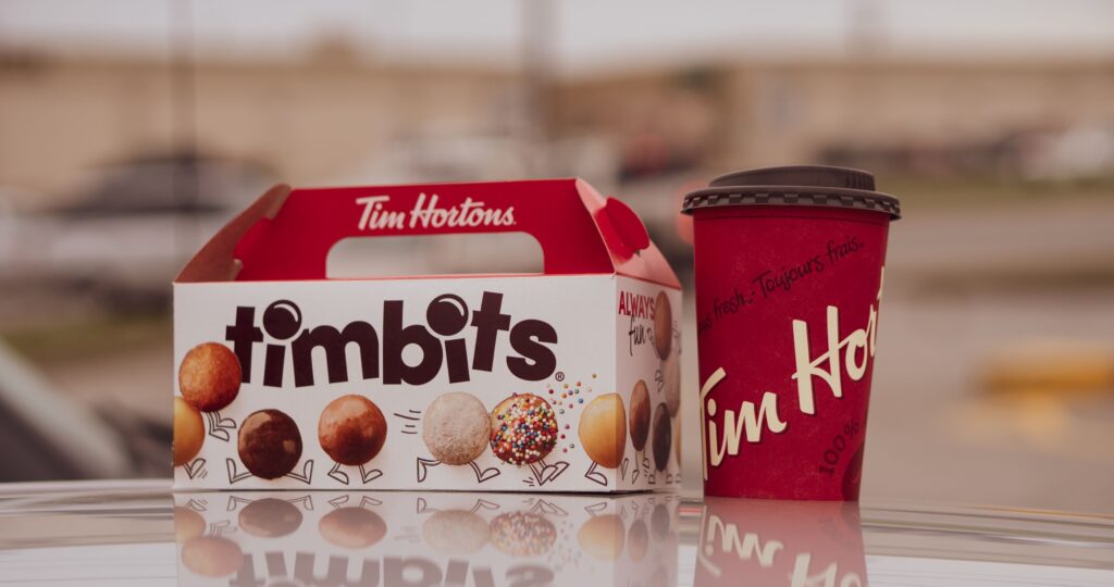 A picture of timbits and a Tim Horton's cup of coffee. The Tim Horton’s Double Double is a hot coffee with two shots of cream and two packs of sugar and is now a huge part of Canadian culture!