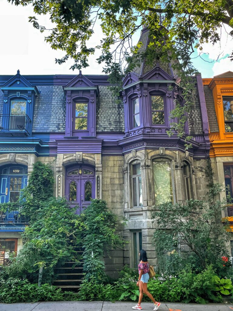 Photo of Canoo member walking in front of gothic style houses with blue, purple, and orange doors in Montreal.