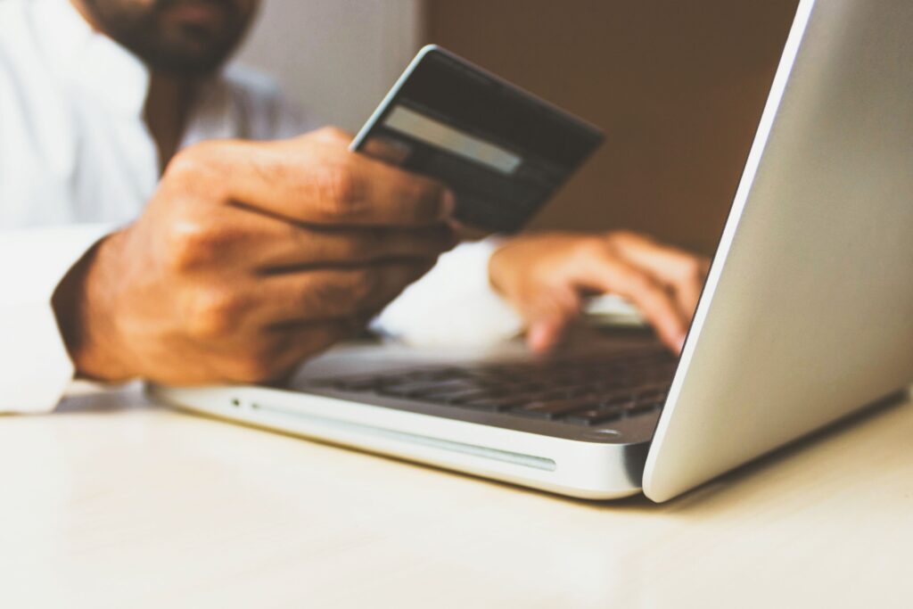 Person holding a credit card in front of a computer as they manage their personal finances.