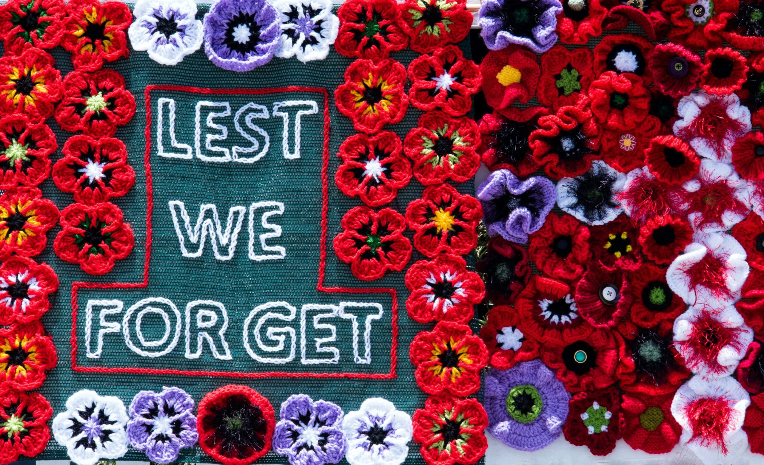 Photo of knit poppies with stitching that says "Lest We Forget".