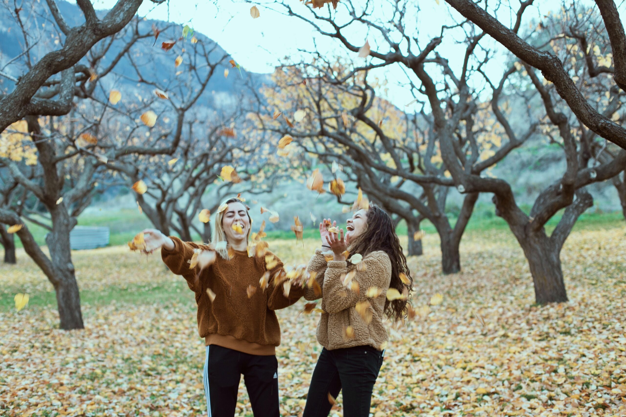 girls throwing autumn leaves in park