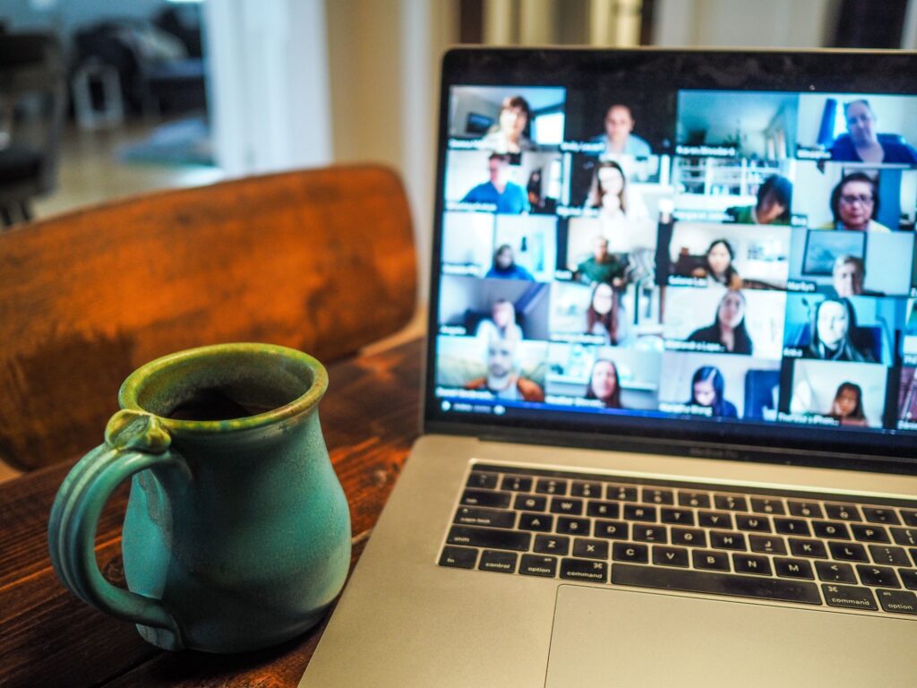 A photo of a computer with a virtual networking meeting displayed next to a cup of coffee.
