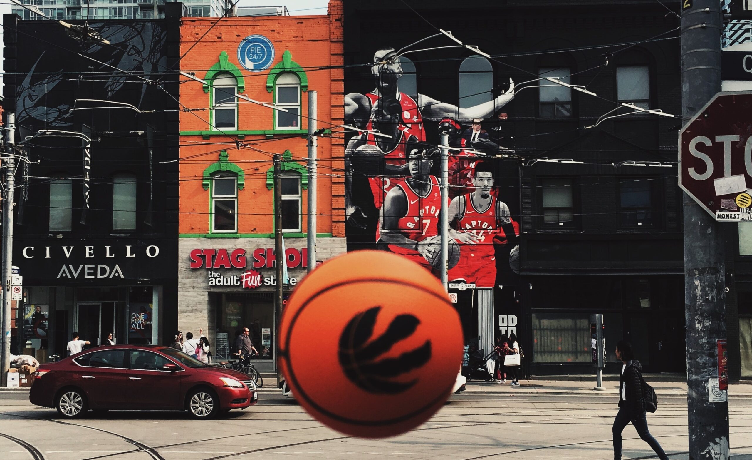 Photo of a basketball in front of buildings in Toronto with Raptors players painted on the exterior wall.