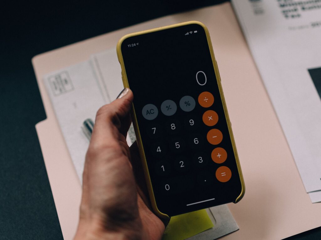 A person holding their phone with the calculator app open on top of a folder of paperwork.