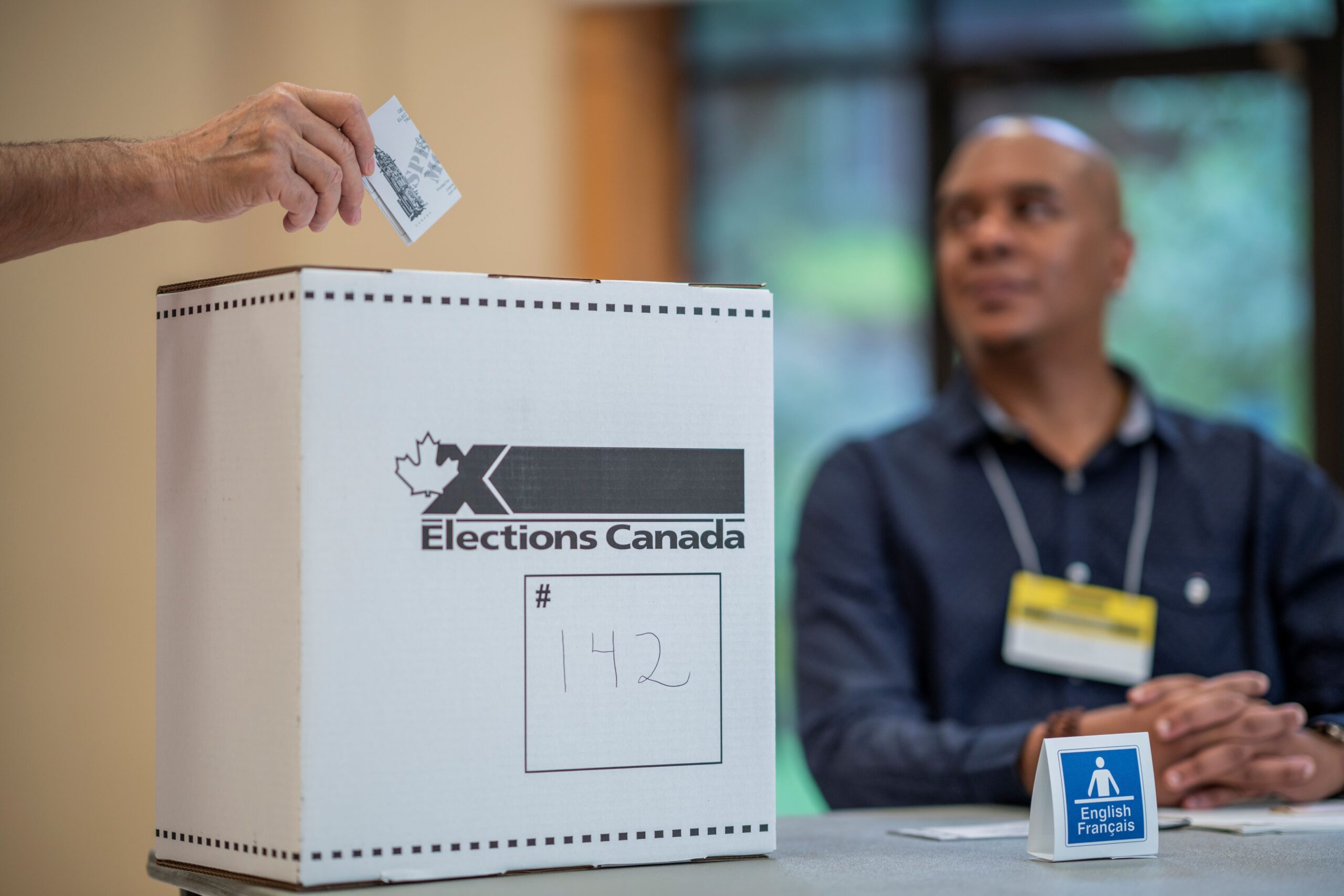 A new Canadian performing work in a federal election as a Canadian puts a vote in a ballot box.