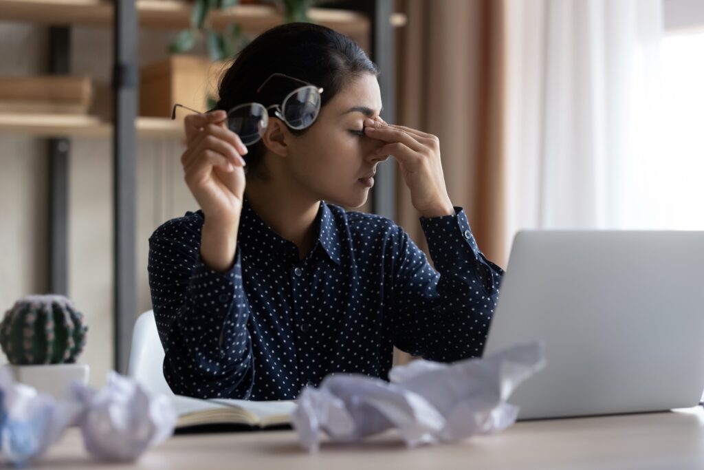 Photo of woman holding her glasses in front of a laptop appeared stressed.