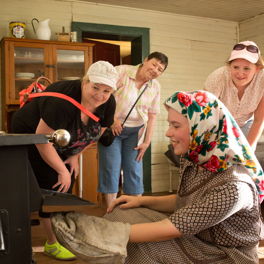 Person open old oven at the Ukrainian Cultural Heritage Village dressed in traditional clothing.