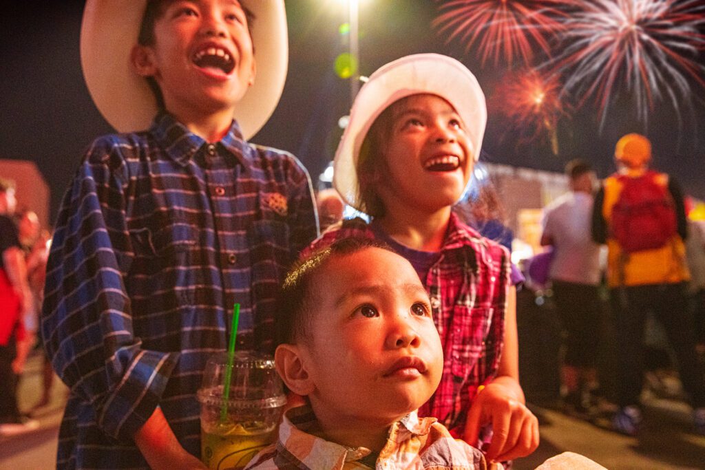 Three children at the Calgary Stampede with fireworks in the background.