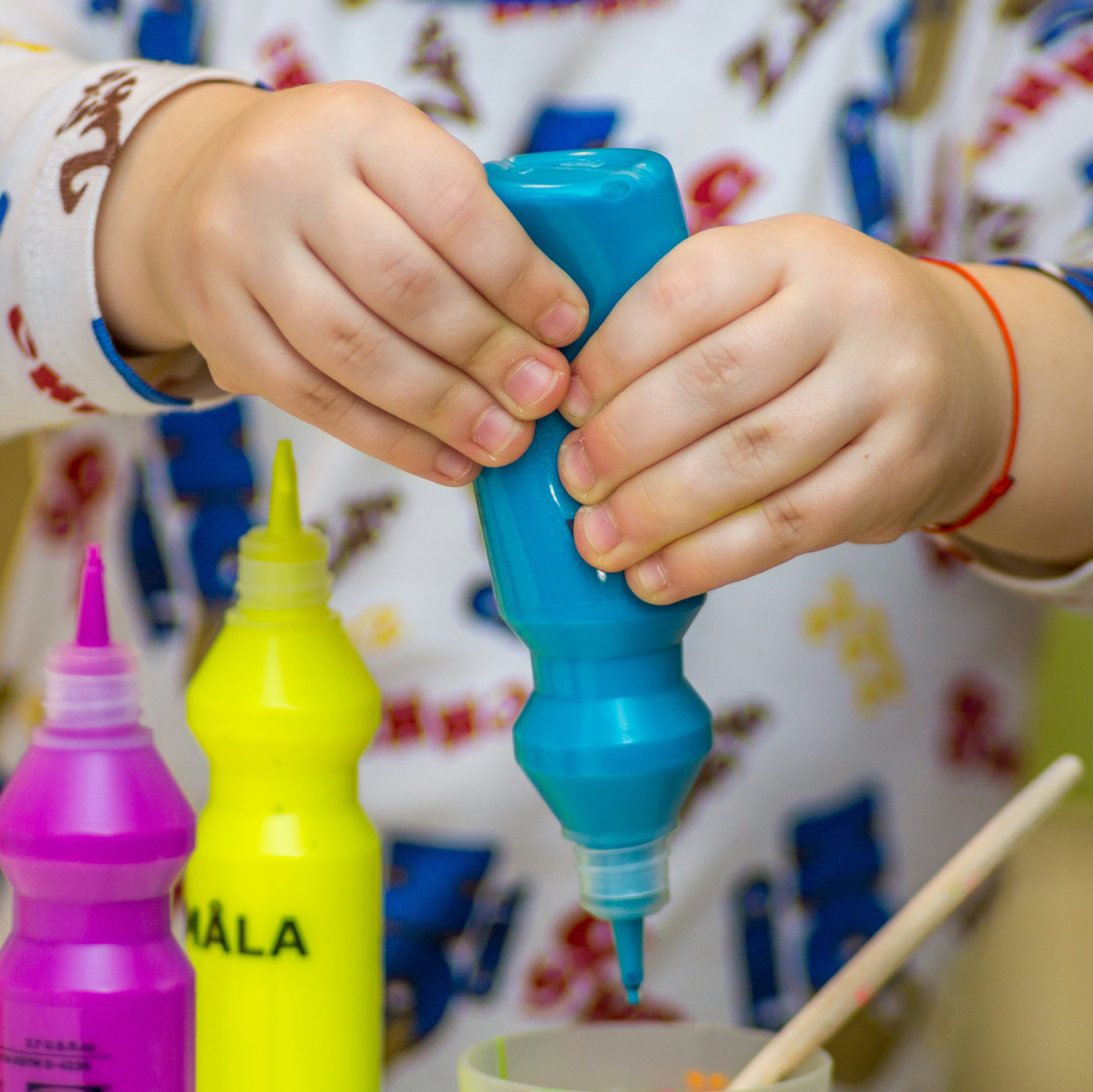 Child squeezing paint bottle while making a craft.