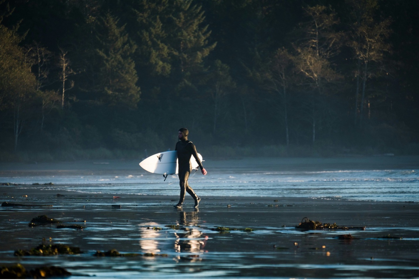 Person carrying their surf board after surfing in Tofino, BC.