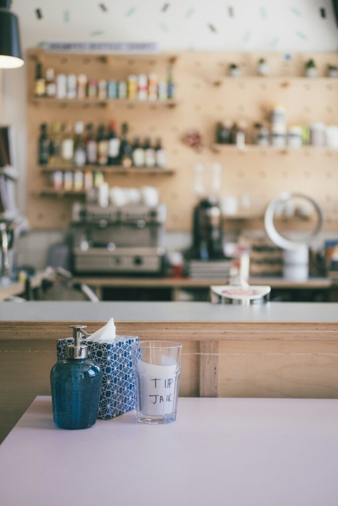 Blue ceramic soap dispenser with a blue tissue and glass with a tip jar label on it on brown wooden table