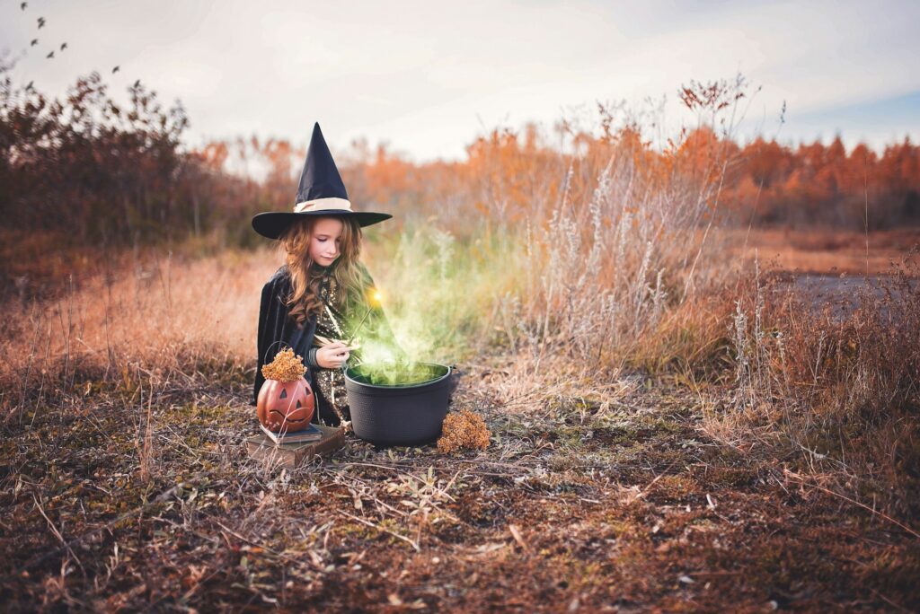 Girl dressed as a witch with a caludron in an open field 