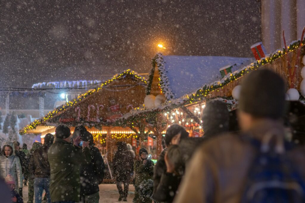 People walking down a snow-covered street which is decorated with fairy lights. 