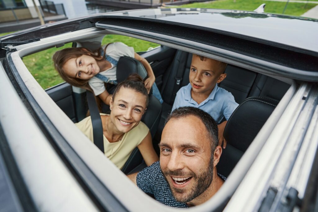 contented man smiling and looking through the sunroof while sitting in a car with his beloved wife and two children