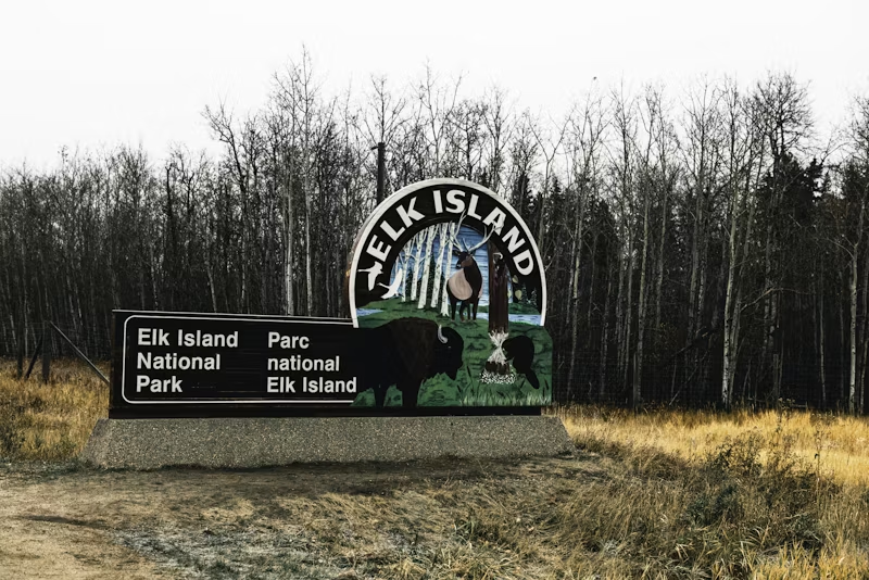 a national park sign that says Elk Island on it in front of a field with trees in the background 