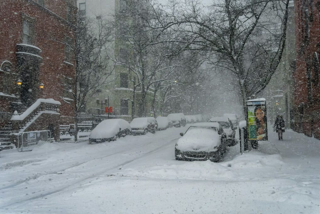 A snowy street with snow-coveredcars parked on the side.