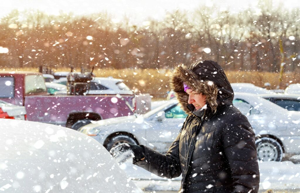 Woman brushing off snow off her car on a cold winter day 