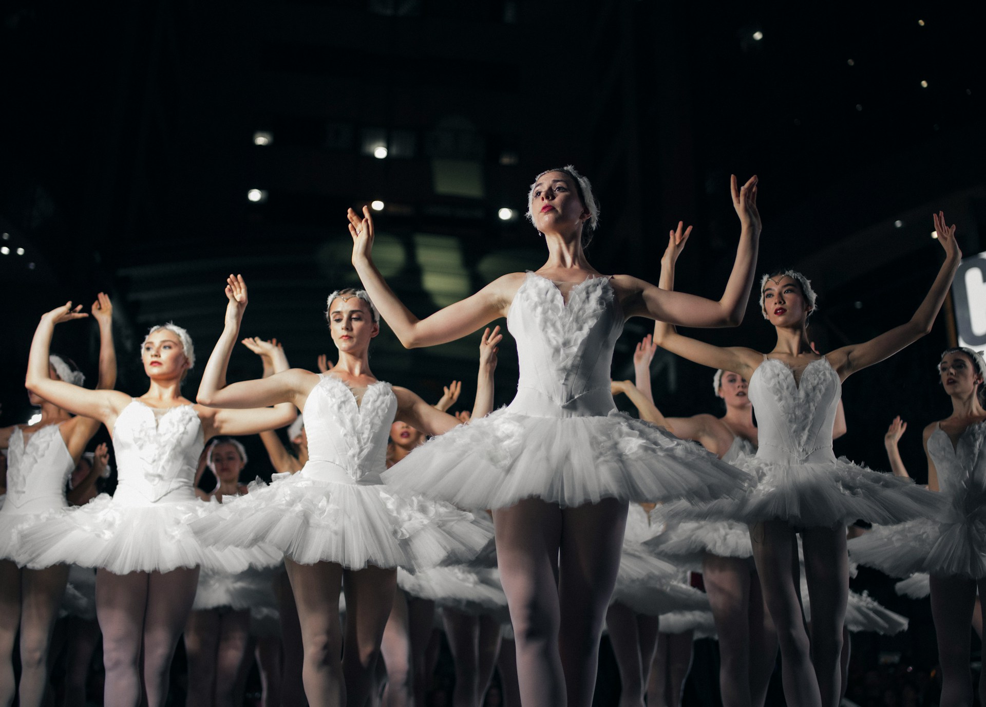 A group of ballerinas performing on stage with both their hands raised