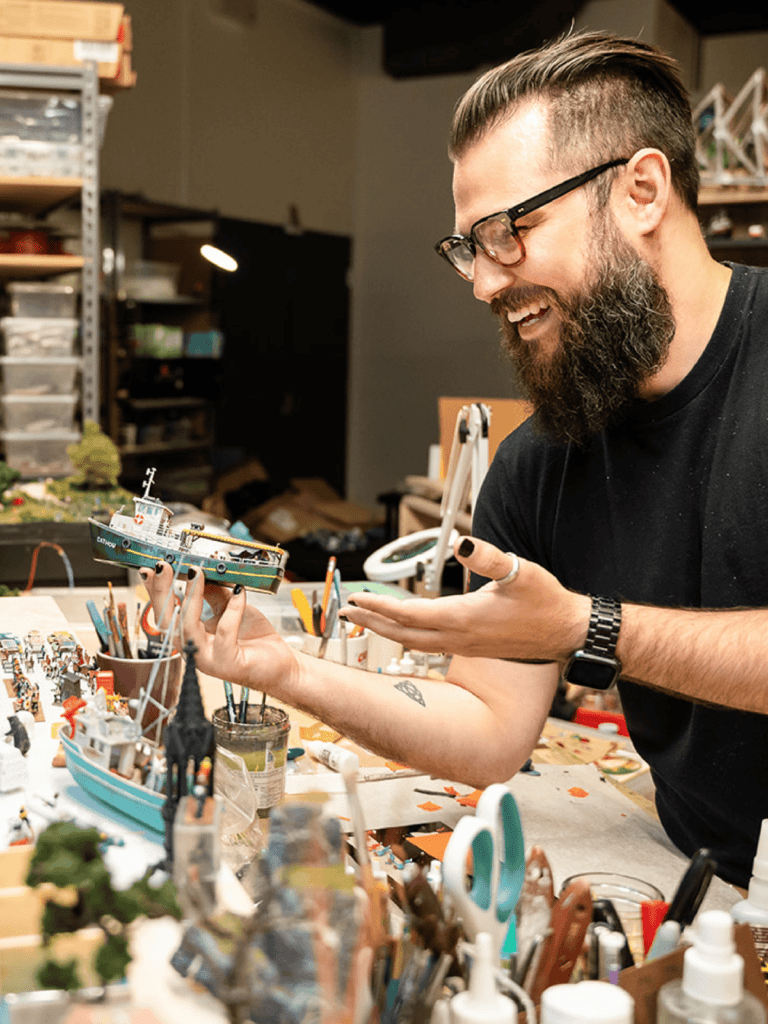 An image of a person holding a miniature boat while working at Little Canada.